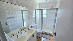 Une salle de bain avec deux lavabos, des toilettes, une douche et un grand miroir.