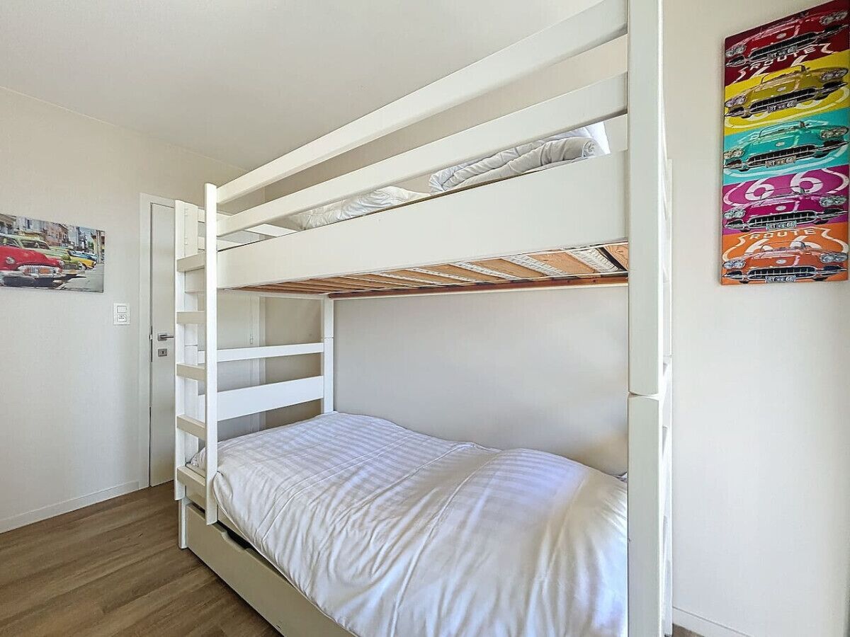 A bunk bed with a white frame and bedding, a door to a bathroom, and a colorful poster on the wall.