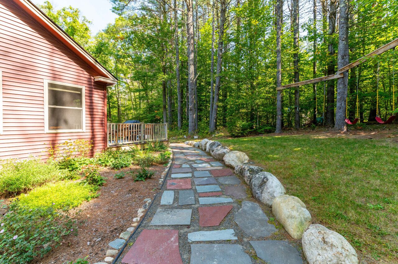 A red cabin with a stone pathway leading to a swing set in a wooded area.