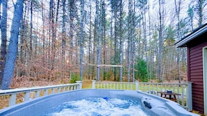 Een hottub omringd door een houten terras met een balustrade, met op de achtergrond bomen en een gebouw.