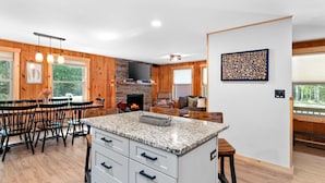 Een moderne keuken met een centraal eiland, houten lambrisering, een open haard en een eethoek met stoelen en een tafel.