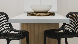 A modern dining area with a white table, two black chairs, a woven basket, and a wooden panel. - Peris #5 w. Yard steps to Bus St. & Old Town (Chania, Crete)