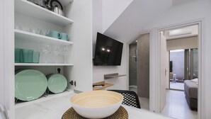 A modern kitchen with white shelves, a large bowl on a woven placemat, and a flat-screen TV mounted on the wall. - Peris #5 w. Yard steps to Bus St. & Old Town (Chania, Crete)