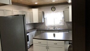 Una cocina con armarios blancos, encimera de granito y techo de madera.