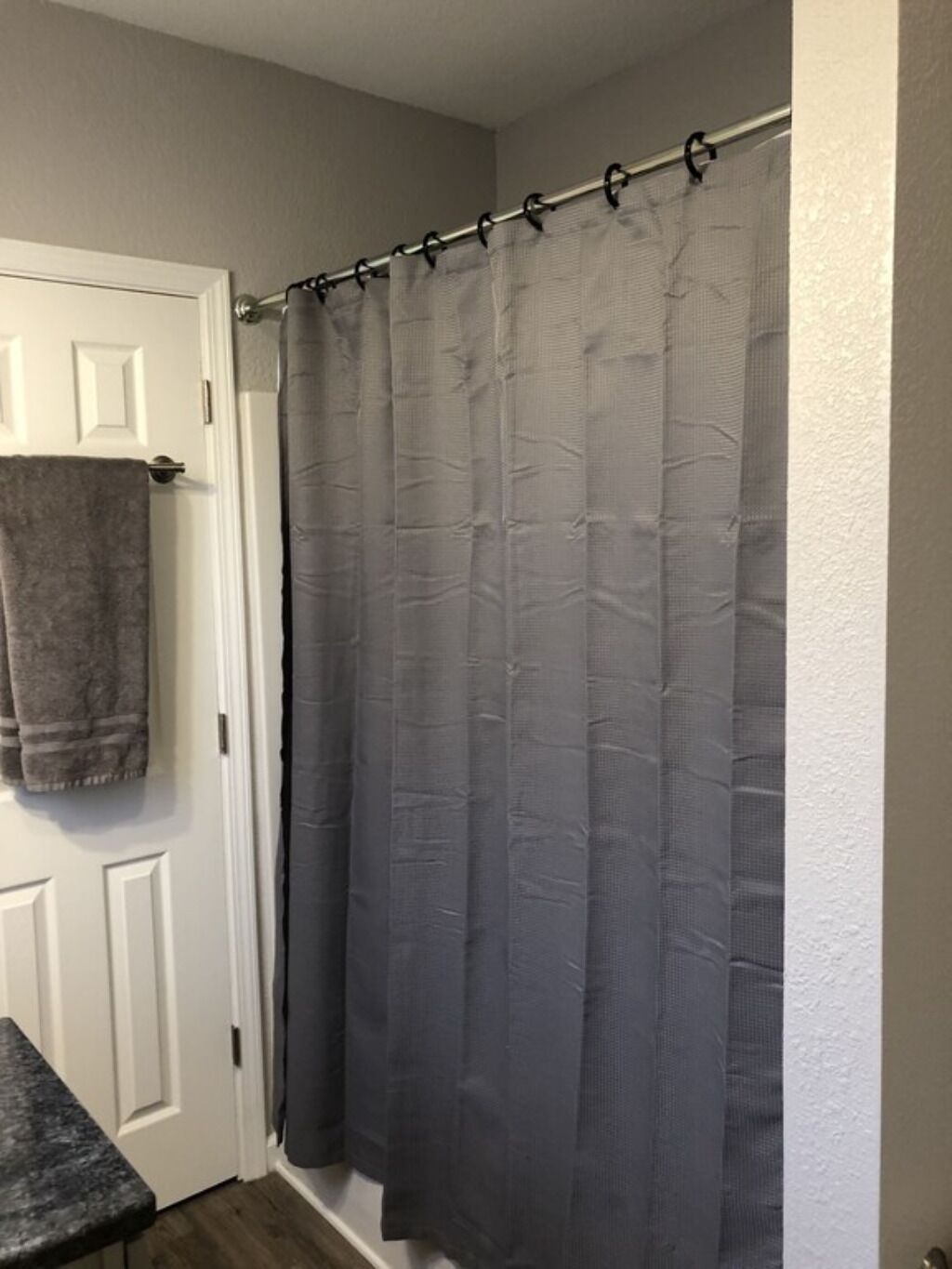 Un baño con cortina de ducha gris, una toalla colgada en la pared y una puerta blanca.