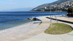 A coastal walkway with a clear view of the sea and a hillside settlement in the background.