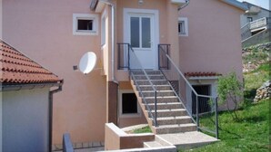 A two-story house with a central door, a small balcony, and a staircase leading to the upper floor.
