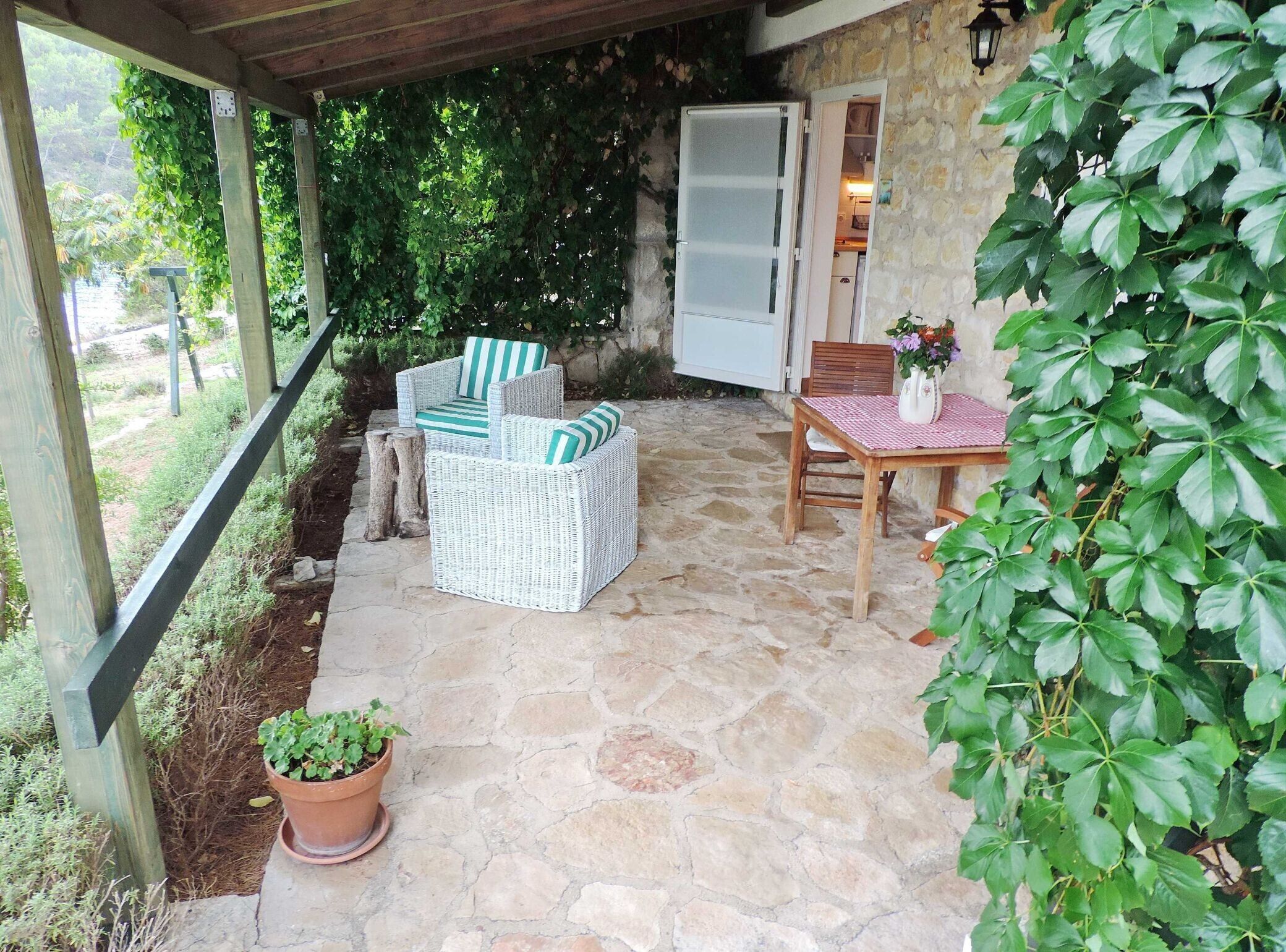 Un patio couvert aménagé avec des meubles en osier, un sol en pierre et une plante en pot.