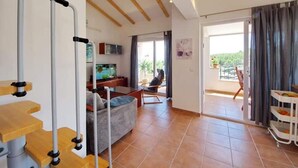 A spacious living area with a sofa, a television, and a balcony with a chair.