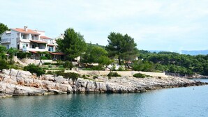 A coastal property with a stone retaining wall, a clear view of the sea, and a multi-story building with balconies.