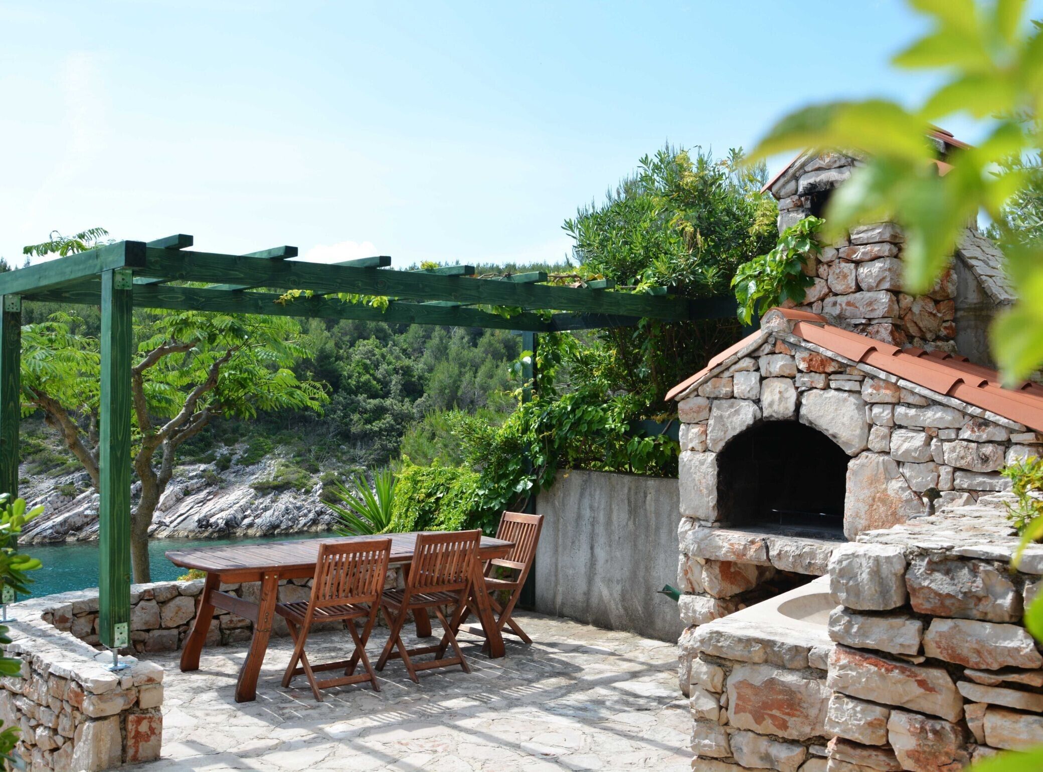 Un área de estar al aire libre construida con piedra, con una pérgola y un horno de piedra.