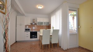 A compact kitchen with white cabinets, a microwave, and an oven. There is a dining table with chairs and a window with curtains. - Brigth and Breezy Rovinj Apartments - Standard One Bedroom Apartment (Rovinj)