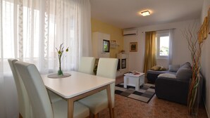 A modern living room with a dining area, a sofa, a TV, and a small kitchen area. - Brigth and Breezy Rovinj Apartments - Standard One Bedroom Apartment (Rovinj)