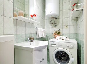 Ein kleines Badezimmer mit Waschbecken, einer Bosch Waschmaschine, einem Handtuchhalter und einem Ablagefach für Toilettenartikel.