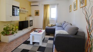 A modern living room with a sofa, a TV, a small table, and a potted plant. - Brigth and Breezy Rovinj Apartments - Standard One Bedroom Apartment (Rovinj)