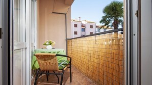 A small balcony with a table and chair, a woven fence, and a view of buildings in the background. - Brigth and Breezy Rovinj Apartments - Standard One Bedroom Apartment (Rovinj)