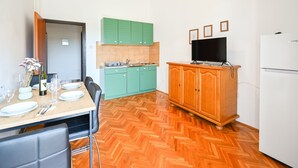Een kleine keuken met groene kastjes, een eettafel gedekt voor twee personen, en een televisie op een houten kast.