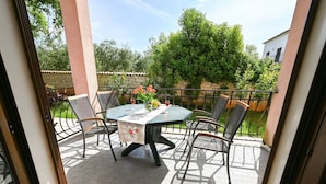 Een balkon met een ronde tafel, vier stoelen en een vaas met bloemen.