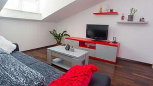 Un salon moderne avec un plafond haut, un téléviseur à écran plat, un canapé gris, un élément de décoration rouge et une petite plante.