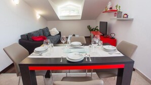Un coin repas avec une table dressée pour quatre personnes, un canapé, un téléviseur et une petite étagère ornée d’objets décoratifs.