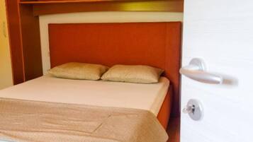 A bed with a beige blanket and pillows, a wooden headboard, and a door with a silver handle.