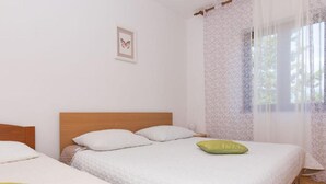 Un dormitorio con dos camas, cabeceros de madera, un cuadro enmarcado en la pared y una ventana con cortinas estampadas.