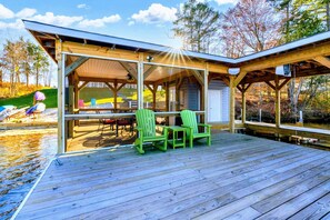 A covered deck with green chairs and a table, overlooking a body of water.