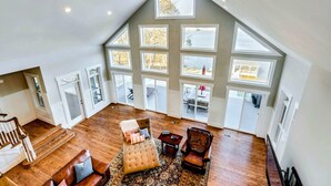 A spacious loft with a high ceiling, large windows, a wooden staircase, and a cozy seating area.
