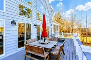 A wooden deck with a table and chairs, a red umbrella, and a white railing.