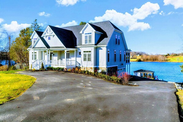 A large, two-story house with a prominent gable roof, a covered porch, and a small dock by a lake.