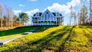 A large, two-story house with a wrap-around porch, a front lawn, and a pathway leading to the entrance.