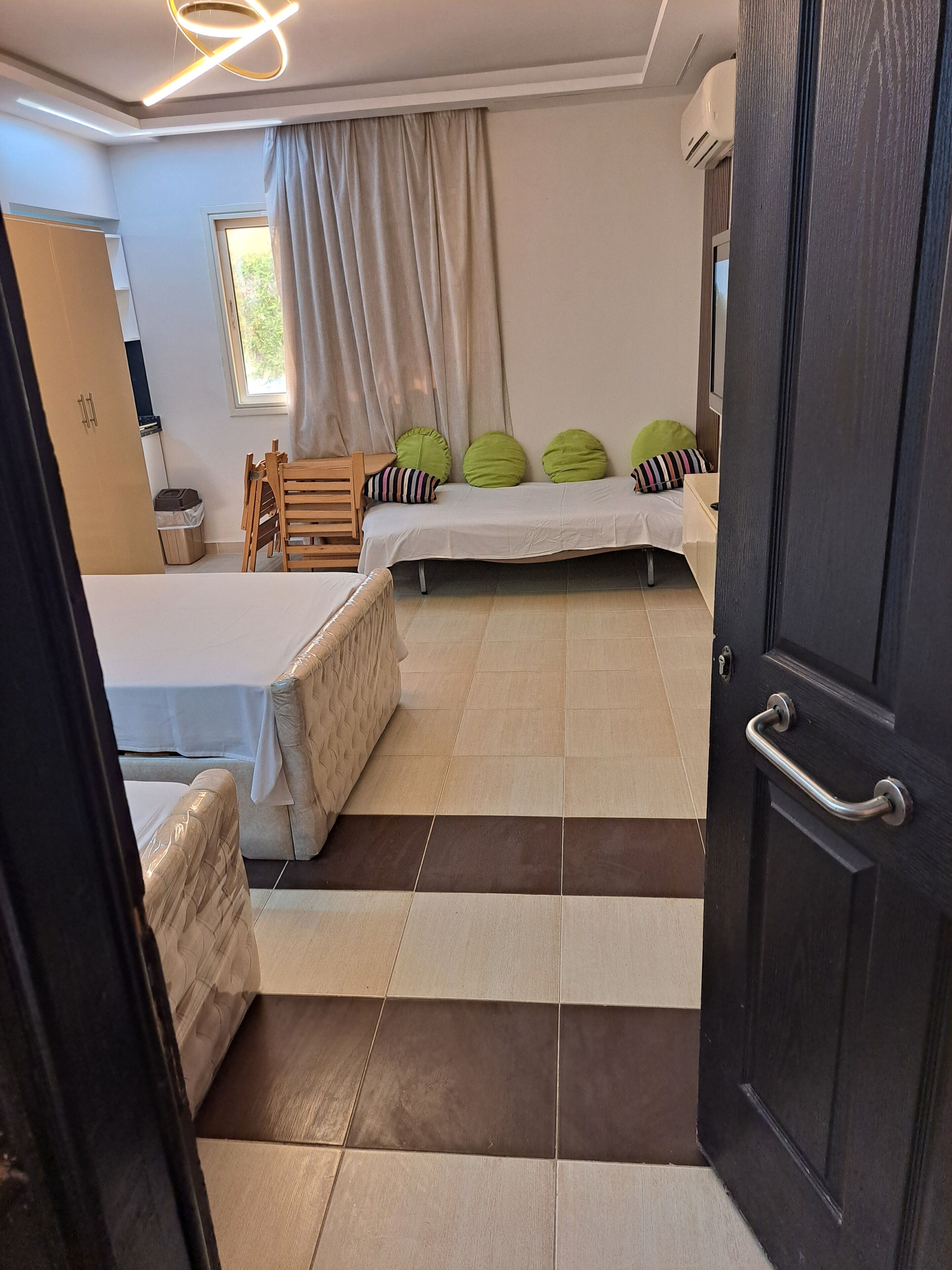 A hotel room with a bed, a sofa, a chair, a small table, a window with curtains, and a door.