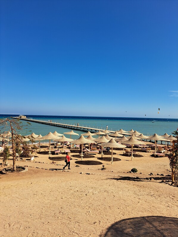 Una playa con sombrillas, sillas de descanso y un muelle que se adentra en el mar.