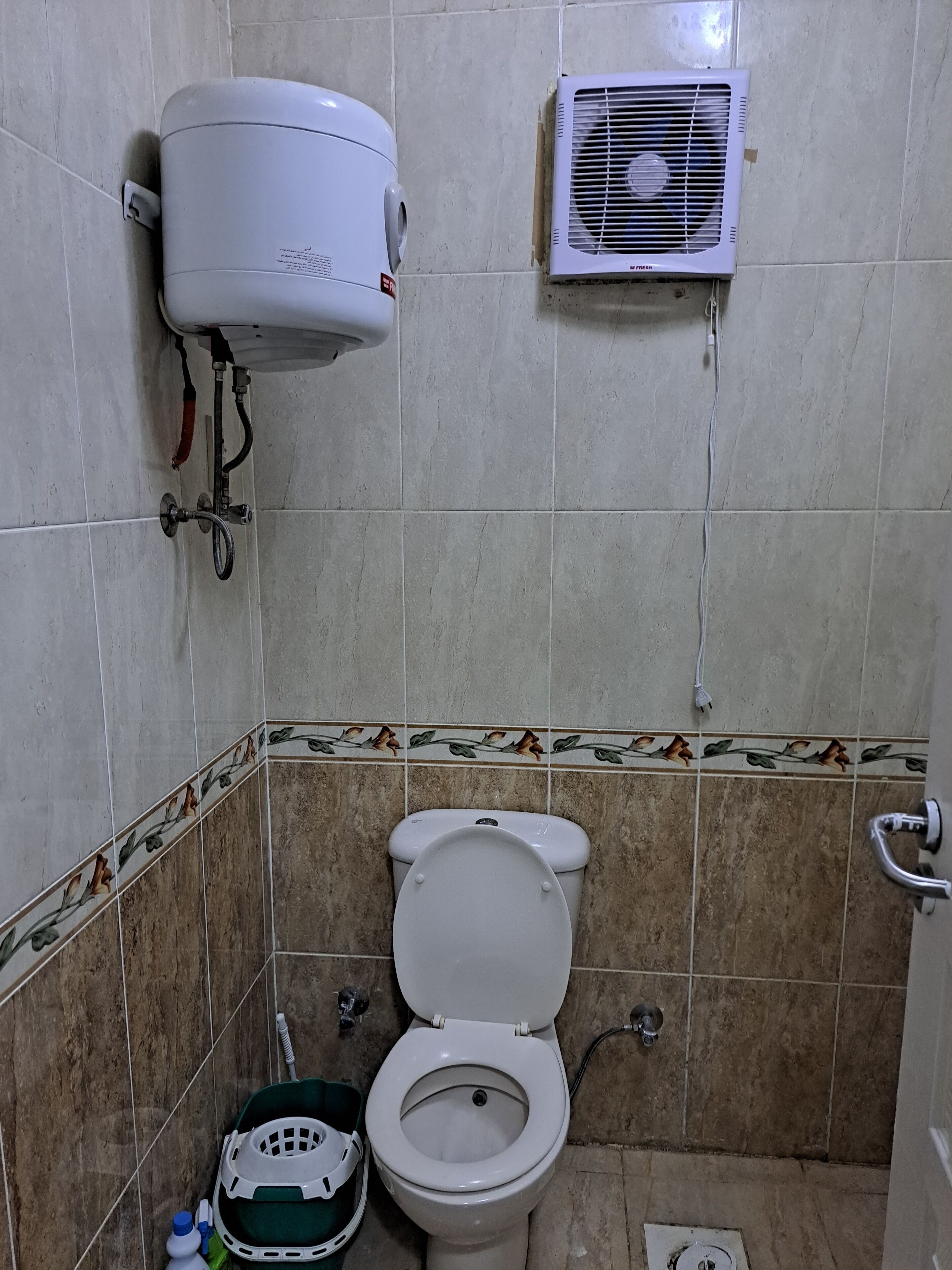 A bathroom with a toilet, a wall-mounted air conditioner, and a shower unit.