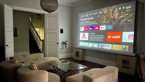 Een woonkamer met een groot scherm waarop een film wordt aanbevolen. Er zijn comfortabele banken en een glazen salontafel.