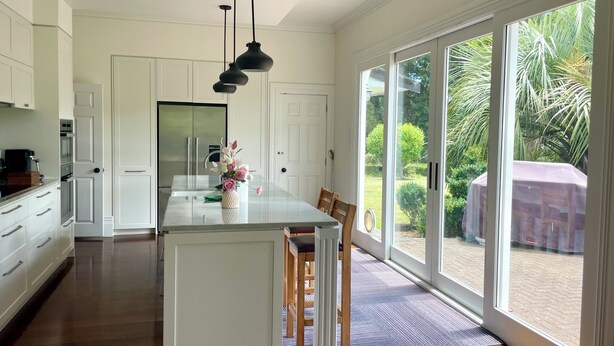Een moderne keuken met een centraal eiland, witte kasten en een grote schuifdeur naar een tuin.