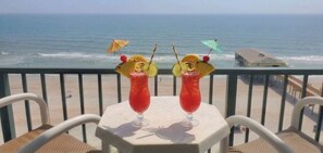 Two cocktails on a table with a view of the ocean and a lifeguard tower in the background. - Oceanfront Daytona Condo with Pool, Hot Tub & Beach Access, Sleeps 6 (Daytona Beach Shores)