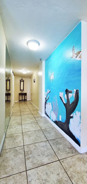 Stunning hallway with a mural of a marine scene, featuring a turtle and underwater plants, leading to a room with a door and a small table with a chair.