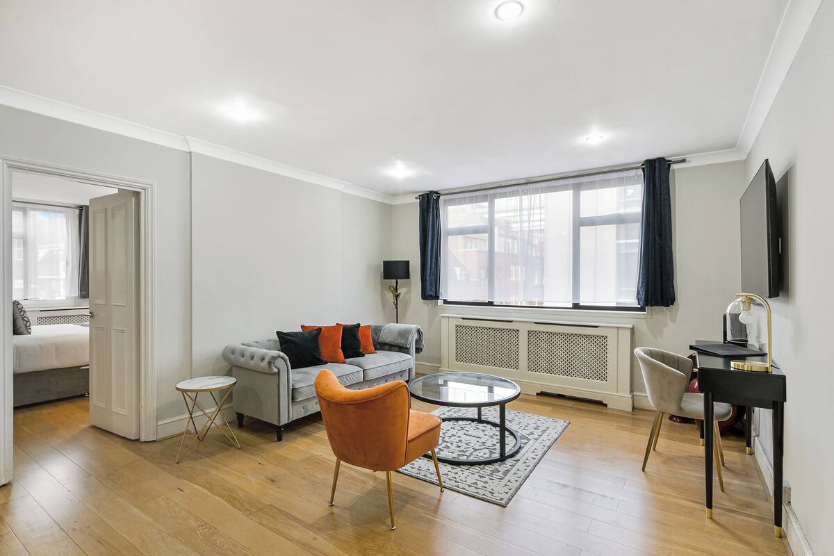 Una sala de estar moderna con un sofá gris, un sillón naranja y una mesa de centro de vidrio.