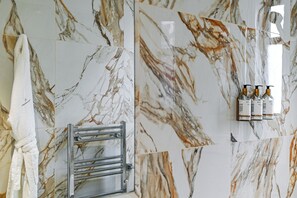 A bathroom with marble tiles, a towel rack, a towel, and three bottles of hand soap. - Avari Apartments - Princeton Collection (London)