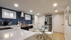 Una cocina moderna con armarios blancos, un refrigerador de acero inoxidable y una mesa de comedor de vidrio con sillas blancas.