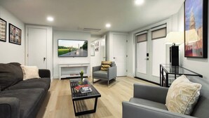Una sala de estar moderna con un sofá gris, un sillón gris más pequeño, una mesa de centro y un televisor de pantalla plana montado en la pared.