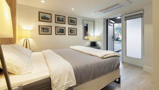 Una habitación de hotel moderna con cama, lámparas de noche, un ventanal grande y cuadros en la pared.