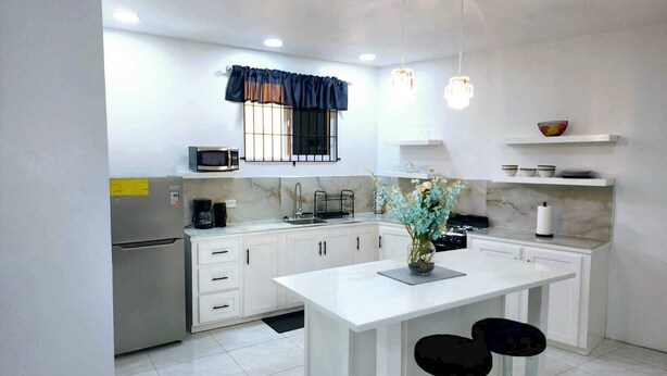 A modern kitchen with white cabinetry, a central island with bar stools, a microwave, and a coffee maker. - Spacious, modern 2-bedroom apartment, Westend Negril with AC, WiFi, W/Heater (Negril)