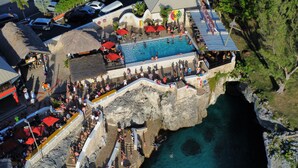 A resort with a pool, a rocky cliffside, and a restaurant area. - Spacious, modern 2-bedroom apartment, Westend Negril with AC, WiFi, W/Heater (Negril)