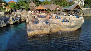 A resort with a large rock formation, clear blue water, and outdoor seating areas. - Spacious, modern 2-bedroom apartment, Westend Negril with AC, WiFi, W/Heater (Negril)