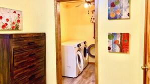 Een wasserette met een wasmachine en droger, houten kasten en twee aan de muur hangende kunstwerken.