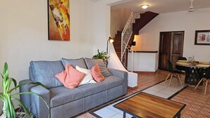 A living room with a grey sofa, a wooden coffee table, a staircase, and a dining area with a round table and chairs.