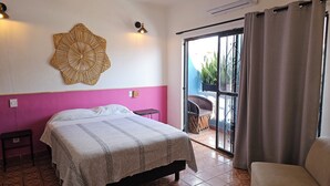 A bedroom with a bed, a small table, a decorative wall hanging, and a view of the outside through a sliding door.