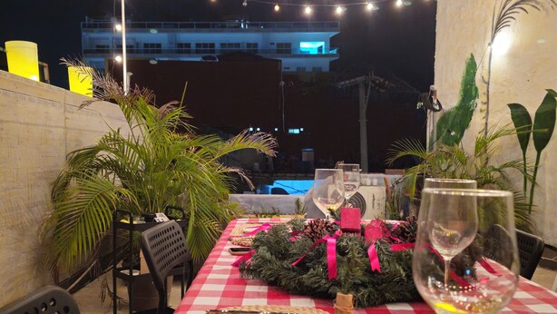 An outdoor dining area with a checkered tablecloth, string lights, and a pool in the background.